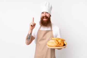 Redhead man in chef uniform. Male baker holding a table with several breads pointing up a great idea