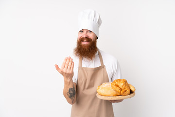 Redhead man in chef uniform. Male baker holding a table with several breads inviting to come with hand. Happy that you came