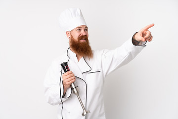 Redhead man using hand blender over isolated white background touching on transparent screen