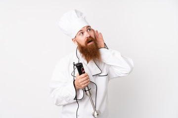 Redhead man using hand blender over isolated white background listening something