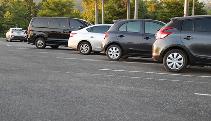 Closeup of rear, back side of dirty black car with sunlight and other cars parking in outdoor parking area in twilight evening.