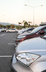 Closeup of front side of bronze car and other cars parking in outdoor parking lot with natural background in twilight evening. Vertical view.