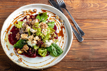 Beetroot carpaccio with walnuts, goat cheese, lettuce and spinach. Dressed with sauce. In a deep plate, on a dark background.