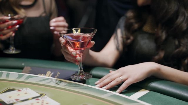 Casino: A bearded man communicates with preatty girls and they smile and laugh. Аlcoholic red champagne in the hands. They are sitting at the pocker table