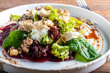 Beetroot carpaccio with walnuts, goat cheese, lettuce and spinach. Dressed with sauce. On a dark background.