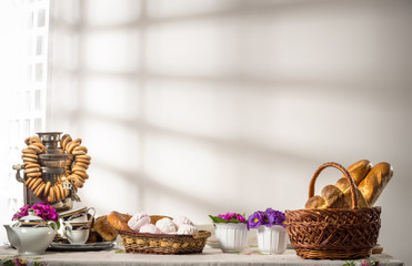 Still life with russian food rolls bagels marshmallows and samovar with tea stands on table on background of white wall in kitchen with sunlight. Concept of Slavic hospitable countries. Copyspace