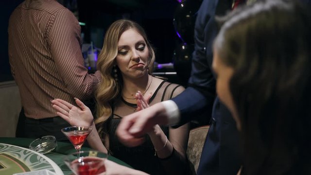 Casino: A bearded man communicates with preatty girls and they smile and laugh. Аlcoholic red champagne in the hands. They are sitting at the pocker table