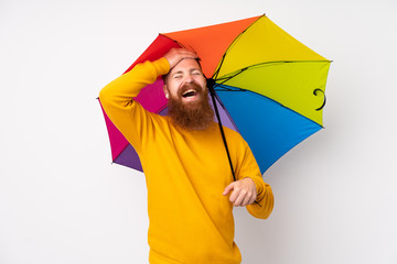 Redhead man with long beard holding an umbrella over isolated white background laughing © luismolinero