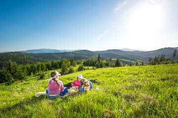 Young mother and little daughters lie on a slope overgrown with grass or admire the gorgeous view of a fox growing on the hills on a sunny warm summer day. Camping and trekking concepts. Copyspace