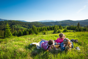 Young mother and little daughters lie on a slope overgrown with grass or admire the gorgeous view of a fox growing on the hills on a sunny warm summer day. Camping and trekking concepts. Copyspace - Powered by Adobe