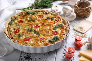 The concept of French cuisine. Kish with mushrooms, tomatoes and cheese on a light wooden background