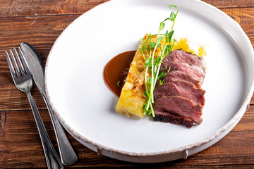 Duck breast with a side dish of potato casseroles, seasoned with pea microgreen with tomato and chili sauce. On a white plate. On a wooden background,