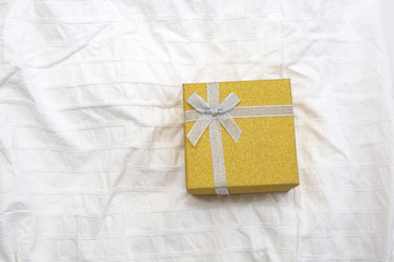 Yellow Gift box. Present box for Holidays on white sheets of a bed Valentine's Day gift, International Women's Day gift over white bed linen background. Valentine's Gift or birthday closeup