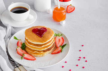 A stack of pancakes with a heart of jam on top with fresh strawberries and mint on a white plate on a light background. Breakfast for Valentine's Day. Horizontal orientation. Copy space.
