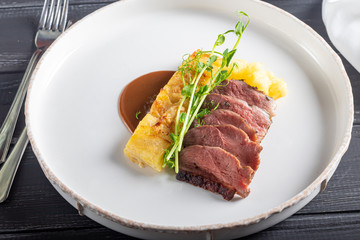 Duck breast with a side dish of potato casseroles, seasoned with pea microgreen with tomato and chili sauce. On a white plate. On a wooden background,