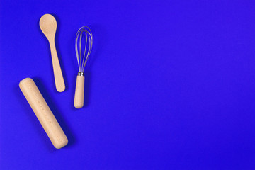Bakeware. Wooden spoon, rolling pin and balloon whisk on blue background. Top view, flat lay