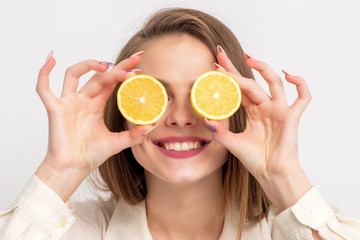 Smiling young woman holding orange pieces like glasses, copy space.