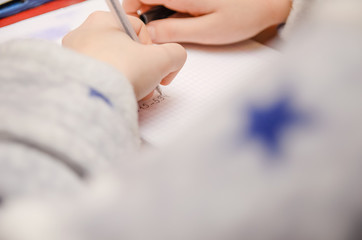 Obraz na płótnie Canvas hand of a child holding a pen and writing a math homework close-up. concept of education