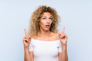 Young blonde woman with curly hair over isolated blue background pointing with the index finger a great idea