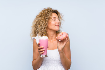 Young blonde woman with curly hair holding a strawberry milkshake and a donut