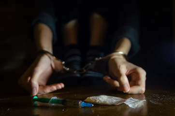 syringe and drugs with a defocused man sitting on the floor and his hands locked in handcuffs.Addict. - obrazy, fototapety, plakaty