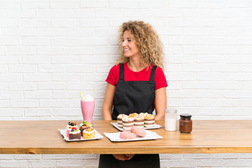 Young woman with lots of different mini cakes in a table looking to the side