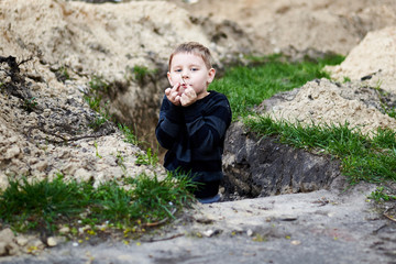 A trench dug in the ground in which a little boy plays.
