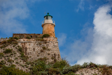 Fototapeta na wymiar Lighthouse on the hill covered with green grass and plants on cloudy blue sky landscape background