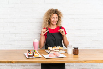 Young woman with lots of different mini cakes in a table proud and self-satisfied