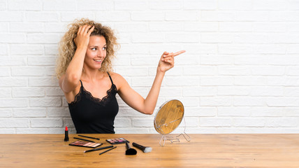 Young woman with lots of makeup brush in a table surprised and pointing finger to the side