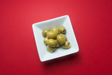 Olives stuffed with pieces of red pepper, in a white bowl, on a red background.