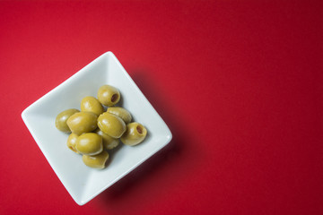 Olives stuffed with pieces of red pepper, in a white bowl, on a red background.