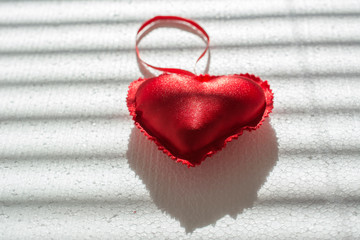 Red heart of plush and play of shadows on a white background. Valentine's day or love concept.
