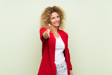 Young blonde woman with curly hair over isolated green background shaking hands for closing a good deal