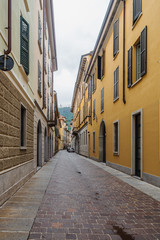 Fototapeta na wymiar View of a narrow, empty street with pastel colorful facades of houses in Como, Italy.