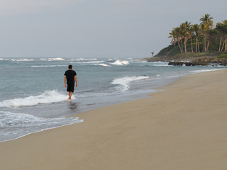 Rear view of a Man Walking On Sandy Tropical Beach at sunset.