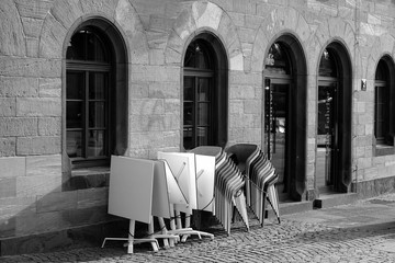 Tische und gestapelte Stühle vor einem alten Café und Bistro mit Rundbogenfenster bei...