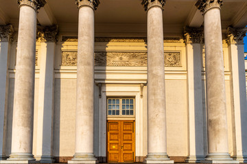 Front view of many massive tall columns and a wooden door entrance to the stone cathedral in Helsinki.