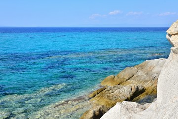 Fototapeta na wymiar Seascape of rocky beach with azure sea water in sunny day. Amazing natural beach with white stones and turquoise water. crystal clear sea with sun reflection. Halkidiki Greece Blue Flag Beach
