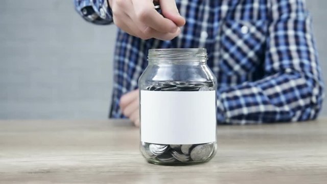 Man counting expenses, putting money into glass jar with empty sticker for note. Saving money concept : Coins in glass jars.
