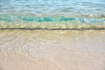 Sea coast with a beautiful soft wave. Transparent blue sea wave with white foam on a clean sandy shore, selective focus. turquoise ocean water. Summertime. Empty sand beach with soft wave background.