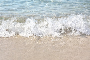 Sea coast with a beautiful soft wave. Transparent blue sea wave with white foam on a clean sandy shore, selective focus. turquoise ocean water. Summertime. Empty sand beach with soft wave background.