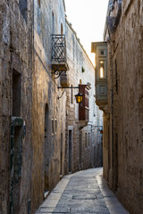 Narrow street between ancient buildings in sun rays of sunset