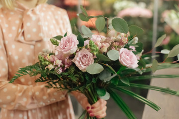 Beautiful smiling female florist in apron arranging bouquet in flower shop