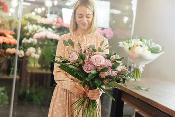 Beautiful smiling female florist in apron arranging bouquet in flower shop