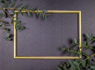Decorative composition, golden photo frame on a gray background, branches with leaves. Flat lay, top view, copy space.