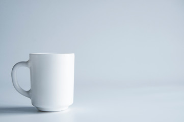 A white porcelain cup stands on a table. On white background