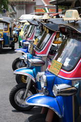 Colorful chrome Thai Tuk Tuk taxi three wheeled motorcycles wait outside The Grand Palace in Thailand to pick up travelers and tourist in busy down Bangkok, Thailand shopping center and cultural hub