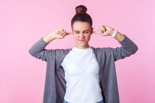 Don't want to listen! Portrait of naughty brunette girl with bun hairstyle in casual clothes covering ears ignoring parental upbringing, disobedient teenager. studio shot isolated on pink background