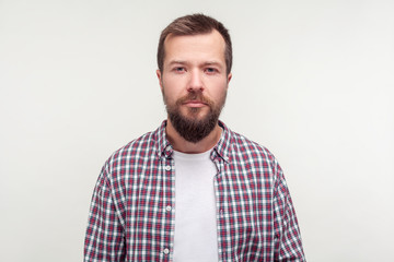 Portrait of serious unhappy despondent young man with beard in plaid shirt looking at camera with...